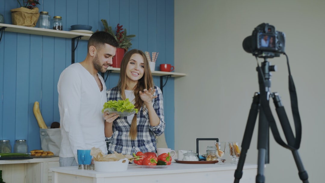 Young attractive couple recording video blog about vegetarian healthy food on dslr camera in the kitchen at home